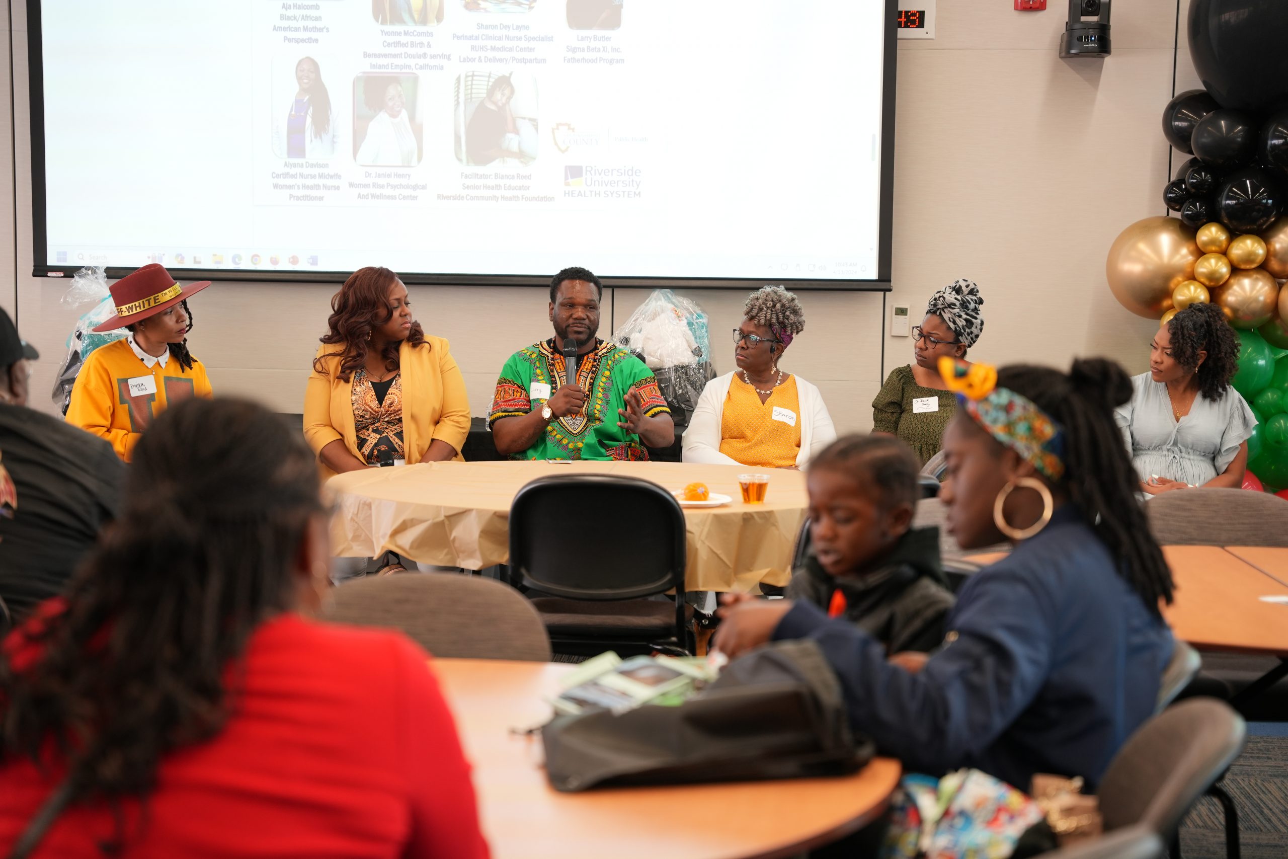 A panel of speakers sitting at the front of a conference room with attendants listening on.