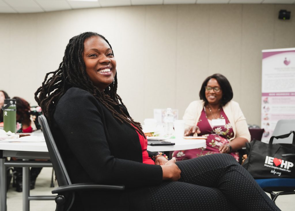 A woman sitting at the front of the event, smiling as she listens to the keynote speaker.