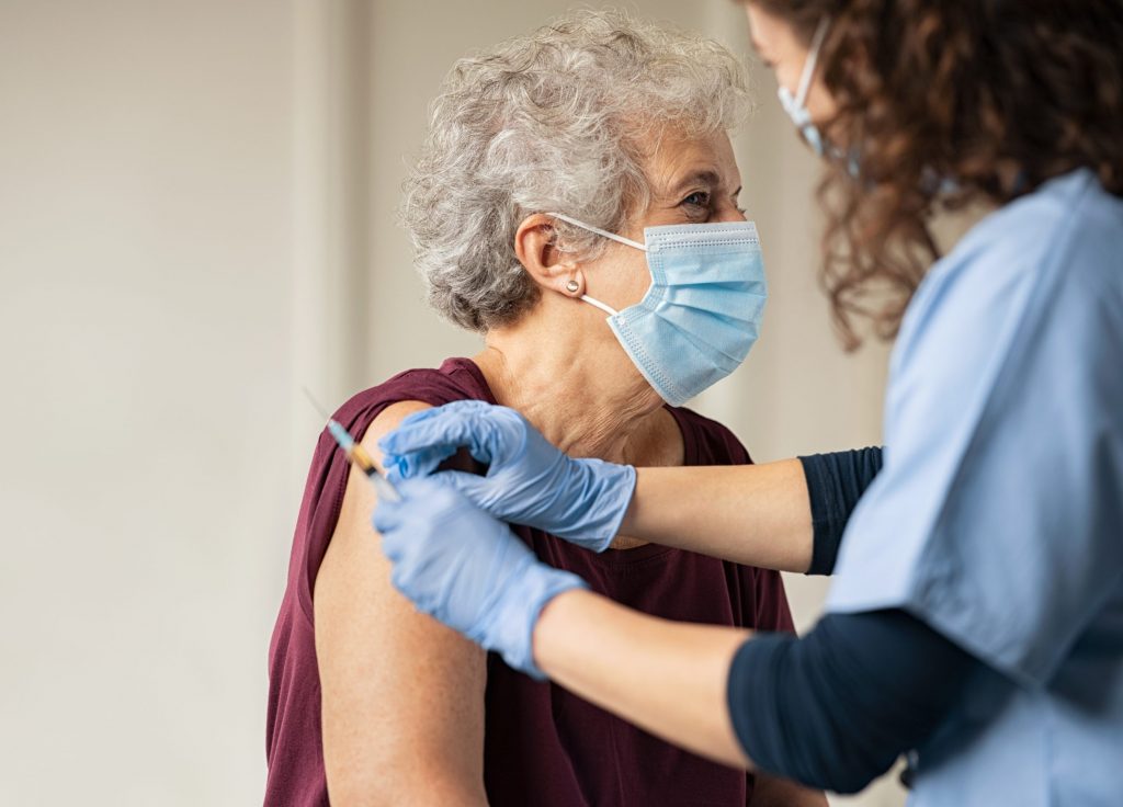 General practitioner vaccinating old patient in private clinic with copy space. Doctor giving injection to senior woman at hospital. Nurse holding syringe and using cotton before giving Covid-19 vaccine.