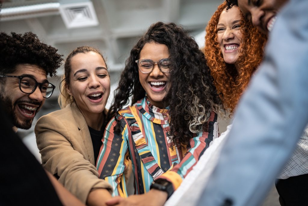 Several individuals from diverse background are joining hands around a circle as they smile.